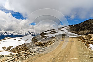 Dirt road in the rocky mountains among snowdrifts on a summer da