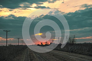 Dirt road surrounded by electricity power lines under a cloudy sky