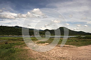 Dirt road track leading toward lake, mountain and clear blue sky. A house is on the other side of the lake