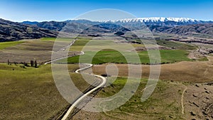 Dirt road winding its way through farmland in a rural valley near the Lindis Pass heading towards the snow capped mountain range