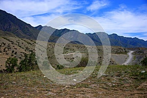 Dirt single-lane road ascending from under the hill from a dry valley into an intermountain basin