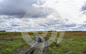 A dirt winding road in an autumn field under the sky with clouds goes to the horizon