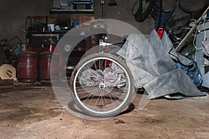 Dirty Bicycle Wheel on the Floor of a Messy Home Garage with Equipment, Workbench, Tools and Cloth in Background