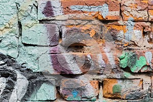 Dirty brick city wall, spattered with colorful spots of bright colors of aerosols