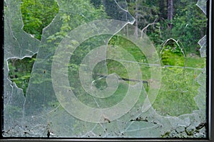 Dirty broken window with a hole in the center, sharp pieces of glass sticking out, concept shot, smash with a stone, military