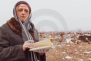 A dirty bum woman reads a book among the garbage