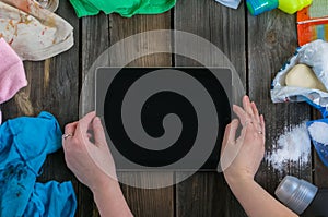 Dirty children`s clothing is scattered on a wooden table next to washing powders and computer tablet in the center.The concept of
