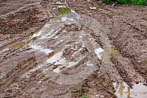 Dirty clay mud crossroads with puddles and tire tracks - close-up with selective focus and linear perspective