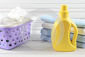Dirty cloth in a plastic purple laundry basket, clean folded cloth and blank yellow detergent bottle on white wood background