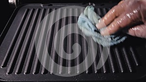 Dirty electric grill. Male hand wiping with cloth grill. Cleaning electric grill dirty plate with rag, detail on man