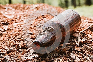 Dirty empty bottle left on sawdust in the Park, clogging the environment