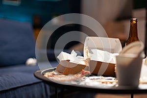 Dirty empty living room with food trash, bottle of beer and napkins on blue sofa