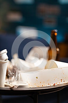 Dirty empty living room with food trash, bottle of beer and napkins on blue sofa