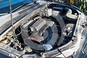 Dirty engine compartment in the used car, visible parts of the engine, cables, lines and reservoirs for liquids.