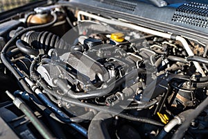 Dirty engine compartment in the used car, visible parts of the engine, cables, lines and reservoirs for liquids.