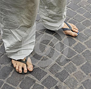 Dirty feet of a man wearing flip flops on the old stone floor.