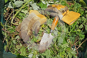 Dirty gardening gloves and trowel in a green waste bag