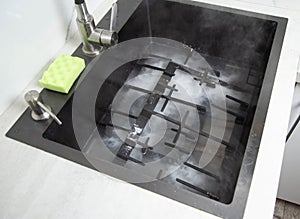 Dirty gas stove grates in the sink with a modern oxygen cleaner for kitchen cleaning. Cleaning the kitchen, removing