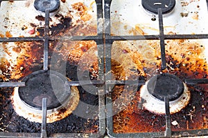 Dirty gas stove surface. Two gas burners and cast iron grate of a gas oven surrounded by old leftovers of food and drinks. Top