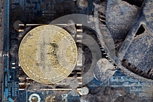 Dirty golden bitcoin inside an old broken computer covered with dust