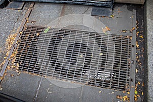 a dirty grate in a pavement next to a metal grill cover