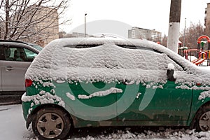 Dirty green compact car in the snow can not go. The first snowfall. cars covered in snow in the city. Transport problems, poorly
