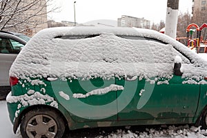 Dirty green compact car in the snow can not go. The first snowfall. cars covered in snow in the city. Transport problems, poorly