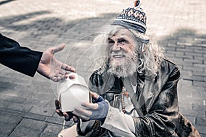 Dirty grey-haired senior homeless wearing ragged clothes and receiving food