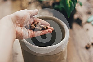 Dirty hand holding drainage  at empty new pot and gardening stylish tools, ground, green plant  on wooden floor. Preparing for