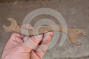 Dirty hand holding one rusty old iron brown open end wrench