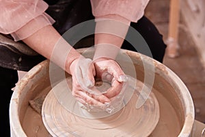 Dirty hands of a ceramist make a cup of clay on a potter& x27;s wheel.