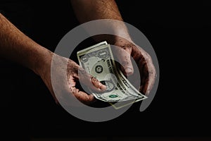 The dirty hands of a homeless man, a poor man holding not much money, dollars. The concept of helping homeless and