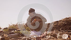 Dirty homeless hungry man in a dump eating orange for lifestyle food in the package with walking goes looking for food