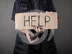 A dirty homeless man stands with a cardboard sign and asks for help