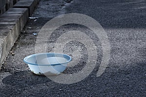 Dirty light blue plastic bowl by the roadside to feed homeless animals.