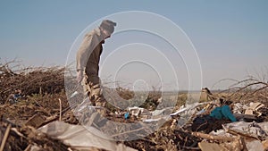 Dirty male homeless hungry man in a dump drinks looking for food in the package with walking goes looking for food slow