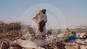 Dirty male homeless hungry man in a dump lifestyle drinks looking for clothing food in the package with walking goes