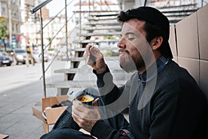 Dirty man is eating corn from can and enjoying it. He is keeping his eyes closed and smiling. Guy is sitting on the