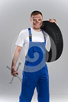 Dirty mechanic standing and holding wrench and tire.