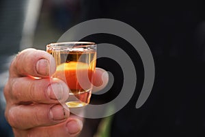 Dirty mens hand holding a shot glass with orange alcohol drink,