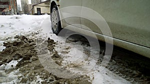 Dirty messy snow near car wheel. Mud, salt and chemicals on road in winter. Ecology problem in city. Protection and wash vehicle