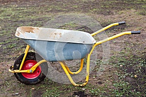 Dirty metal garden wheelbarrow on bare ground