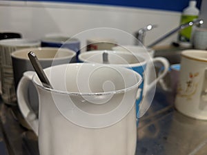 Dirty mugs on a sink draining board with teaspoons in