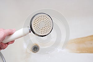 Dirty old shower head close up with limescale and calcified, rusty shower mixer and mould tiles on background, cleaning