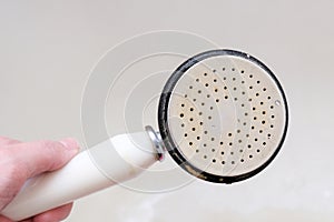 Dirty old shower head close up with limescale and calcified, rusty shower mixer and mould tiles on background, cleaning