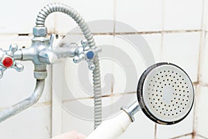 Dirty old shower head close up with limescale and calcified, rusty shower mixer and mould tiles on background, cleaning bathroom