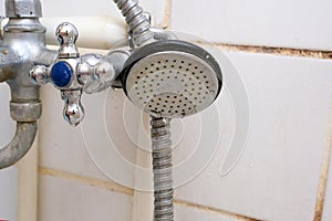 Dirty old shower head with water drops close up with limescale and calcified, rusty shower mixer and mould tiles on