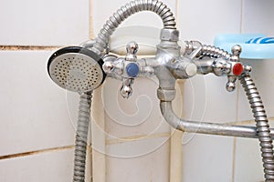 Dirty old shower head with water drops close up with limescale and calcified, rusty shower mixer and mould tiles on