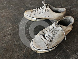 Dirty and old white shoes on dirty cement ground