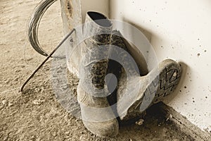 A dirty pair of rubber boots full of dried concrete lies on the unfinished floor of a building under construction